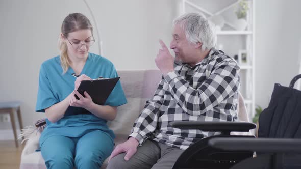 Professional Caucasian Nurse Talking with Elderly Male Patient and Writing Down Symptoms. Elderly