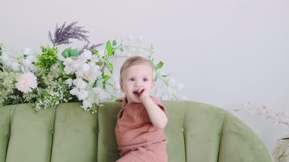 Little boy in a beige suit sits on a green sofa surrounded by beautiful flowers. Happy loving family