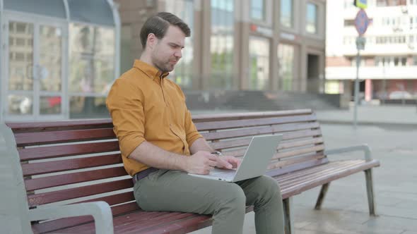 Young Man Reacting to Loss on Laptop while Sitting Outdoor on Bench