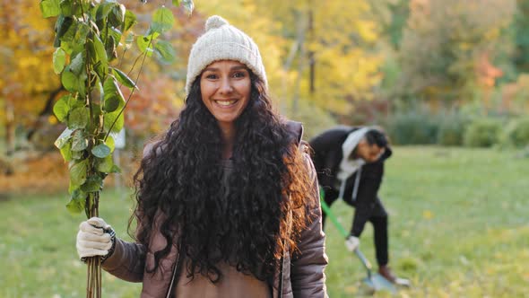 Happy Young Hispanic Woman Standing Outdoors Looking at Camera Holding Sprout in Hand Advertises