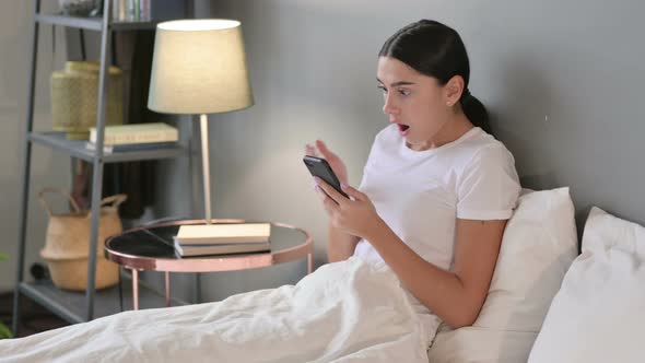 Failure, Latin Woman Reacting To Loss on Smartphone in Bed 