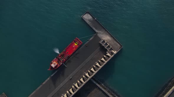 Red cargo ship moored at pier of Tazacorte harbor in La Palma island. Aerial top-down circling