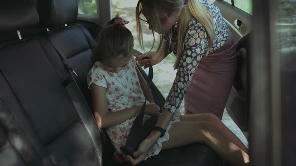 Caring Mother Fastening Girl with Seat Belt in Car