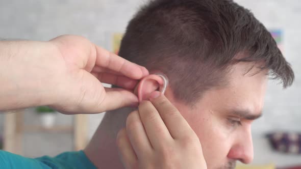 Man Inserts a Hearing Aid Into Her Ear