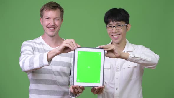Two Happy Young Multi-ethnic Businessmen Showing Digital Tablet To the Camera Together