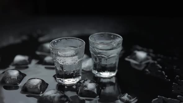 Add Ice Cubes To Shot of Vodka in Glass Against Black Background. Alcohol Drink