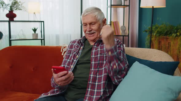 Overjoyed Senior Grandfather Man Hold Smartphone Excited About Mobile App Sport Bet Bid Win at Home