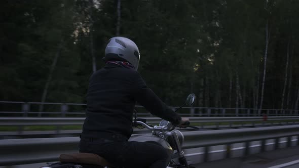 Man Riding Scrambler Motorbike on the Highway Through the Forrest at the Sunset