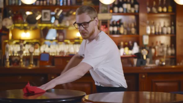 Young Waiter in Workwear Wiping Table with Duster Preparing for New Guests