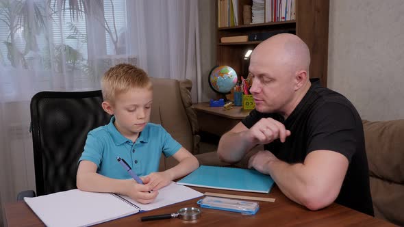 A Father Helping His Son with Homework While Sitting at the Table at Home