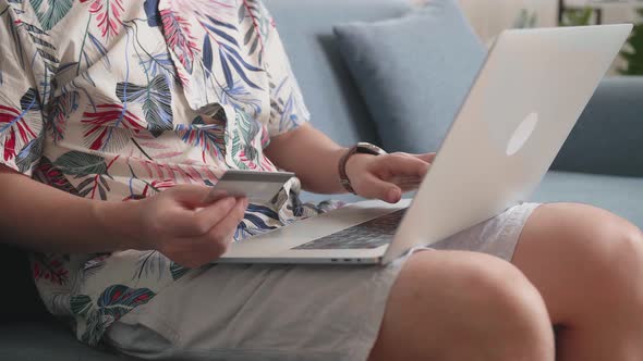 Close Up Of Hand Holding Credit Card And Using Laptop Computer Shopping Online In Living Room