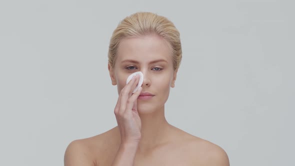 Studio portrait of young, beautiful and natural blond woman applying skin care cream. F