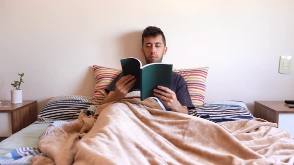 Bored Man Trying To Read A Book In Bed. full shot