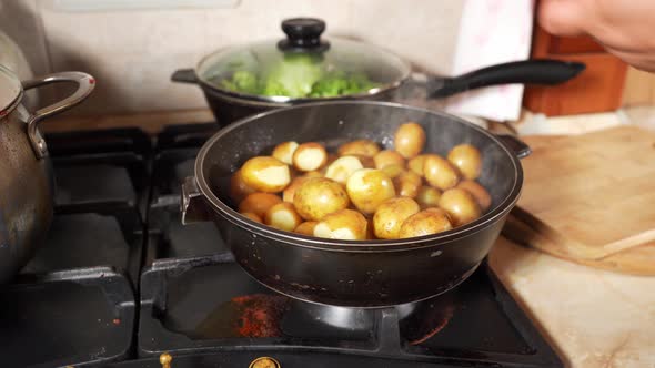 Womans Hand Opens The Lid Of A Frying Pan With Potatoes. Oil Splashes Fly