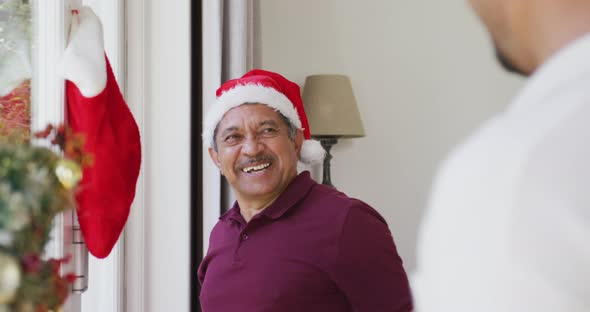 Cheerful senior man hanging christmas sock on window and patting son at home