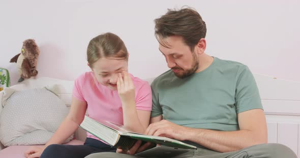Father and Teen Daughter are Sitting on the Sofa and are Looking at the Photo Album The Girl Laughs