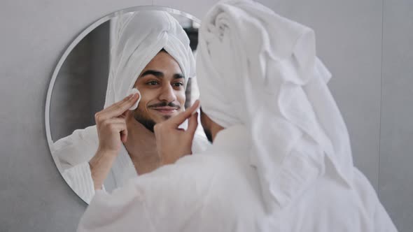 Arabic Indian Bearded Man with Bath Towel on Head Looks in Mirror in Bathroom Smears Face with