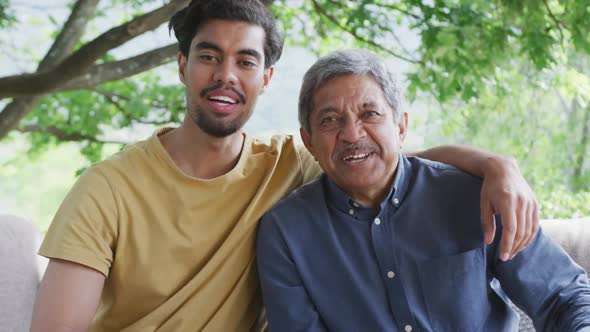 Portrait of happy biracial father and son sitting together at patio