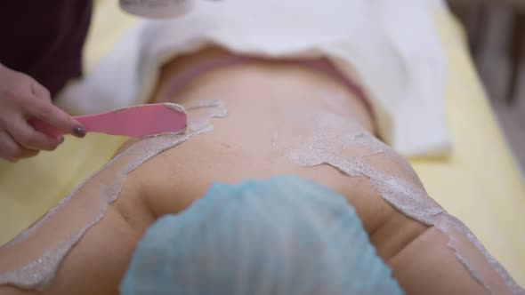 High Angle View of Unrecognizable Relaxed Woman Lying in Beauty Spa with Beautician Applying Peeling