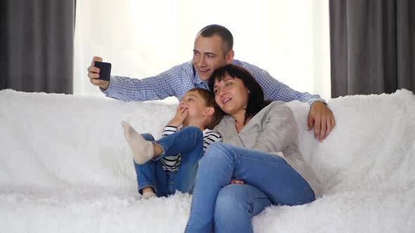 A Man Photographs His Family on a Smartphone Camera. Dad, Mom and Little Son Demonstrate Emotions