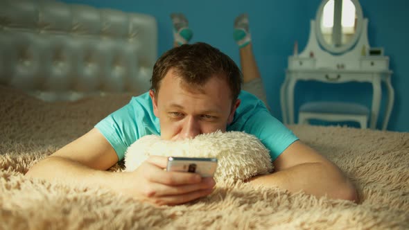 Man with a mobile phone in the morning lies on the bed, front view, lies in front of the camera
