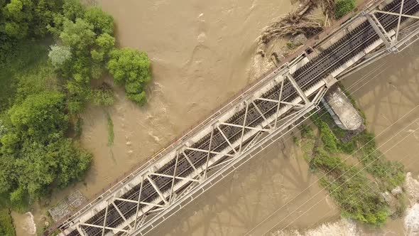 Aerial view of railway metal bridge over dirty river with muddy water in flooding period during