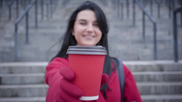 Unrecognizable Blurred Caucasian Woman Stretching Coffee Cup To Camera and Smiling. Young Lady in