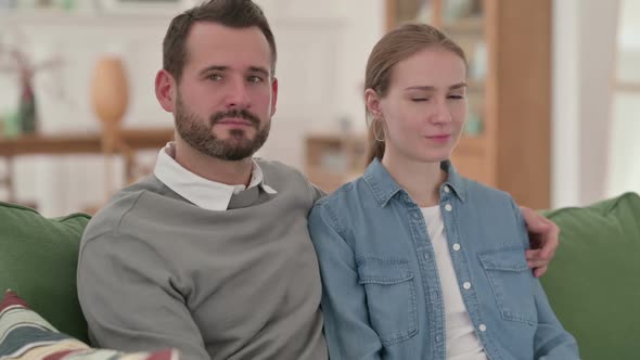 Serious Couple Looking at the Camera While Sitting on Sofa