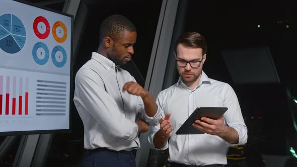 Two colleagues discussing a business project using a digital tablet near the screen