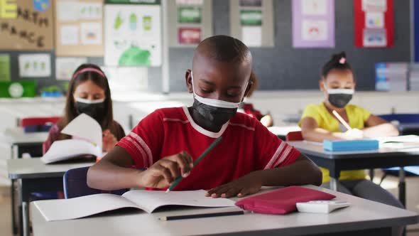 African american boy wearing face mask while studying in the class at school