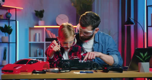 Man and Teen Boy Both in Glasses Soldering Toy Car's Wires or Details Using Soldering Iron at Home