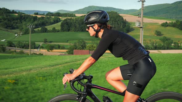 Portrait of pro female cyclist on bicycle. Fit muscular woman athlete riding bike uphill at sunset