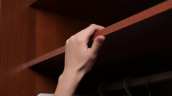 female hand takes and then puts cash savings in dollars on a shelf in a wardrobe