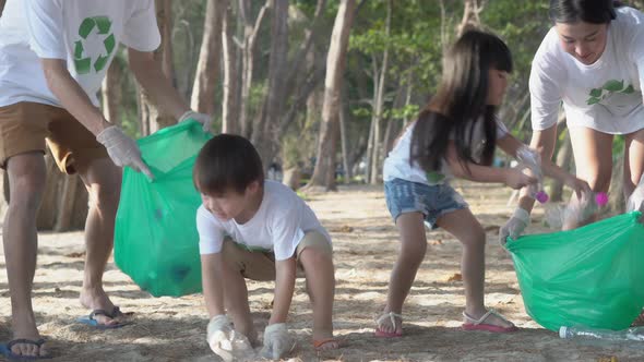 Asian family team volunteer keeping garbage and plastic bottle while cleaning on beach.