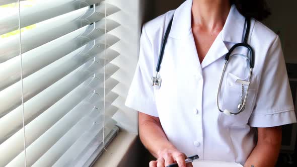 Female doctor holding clipboard and looking through window