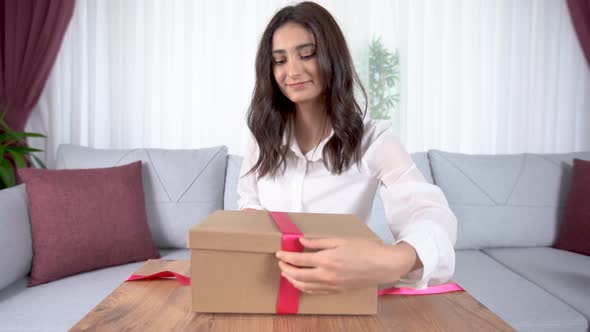 The woman is tying the gift box with a ribbon.