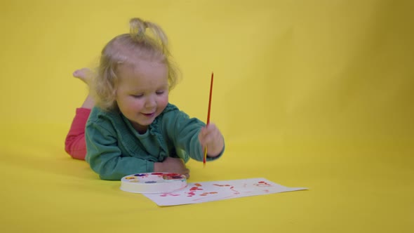 Adorable Toddler Girl Picks Up Paint on Palette and Draws Happy Childs Picture