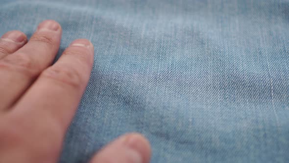 The hand gently touches the denim light blue fabric in motion, assessing tactilely