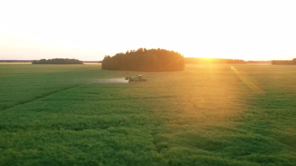 Aerial Follow Farm Tractor Sprays Mineral Water On Agricultural Field At Sunset