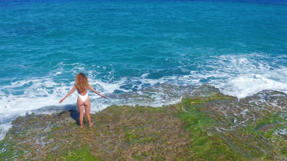 Aerial View. Sexy Girl Standing on the Cliff on the Rocky Beach. A Woman Looks Into the Distance.