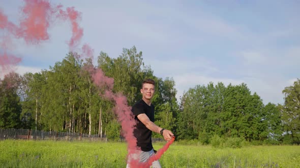The Guy Sprays Colored Red Smoke in the Meadow on a Summer Day