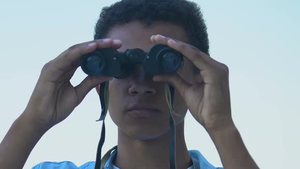 Afro-American teen boy watching through binoculars