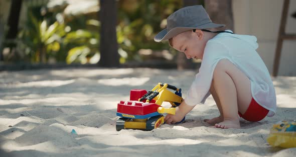 Child Plays with a Plastic Car in the Sand on the Beach