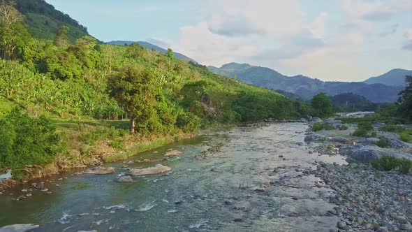 Drone Flies Over Rocky River Running Against Green Hills Sky