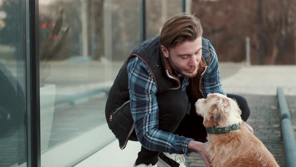 Young Man Sitting with Lovely Dog Outside Near Glass Building