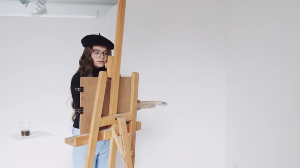 Young Woman Artist in Beret Painting Picture on Canvas in Art Studio