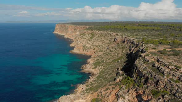 Drone footage flying over the ocean towards the cliffs with blue and turquoise water underneath. Fil