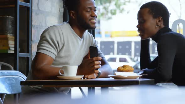 Couple interacting with each other while using mobile phone in cafe 4k
