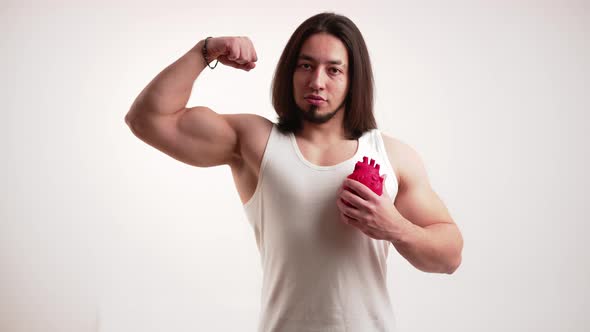 Caucasian Muscular Man with Long Dark Hair and Beard Pumping Fake Anatomical Heart in One Hand and
