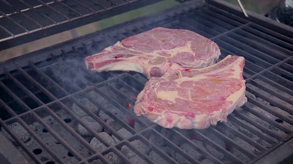 Zoom in view of aged, well marbled raw steaks on a charcoal barbecue.